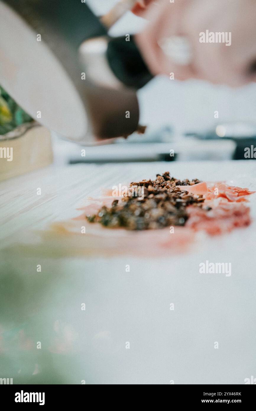 Eine Person kocht Essen mit einem Löffel in einer Pfanne. Das Essen ist mit Gewürzen bedeckt und er ist eine Mischung aus verschiedenen Zutaten. Wärme und Tragekomfort Stockfoto
