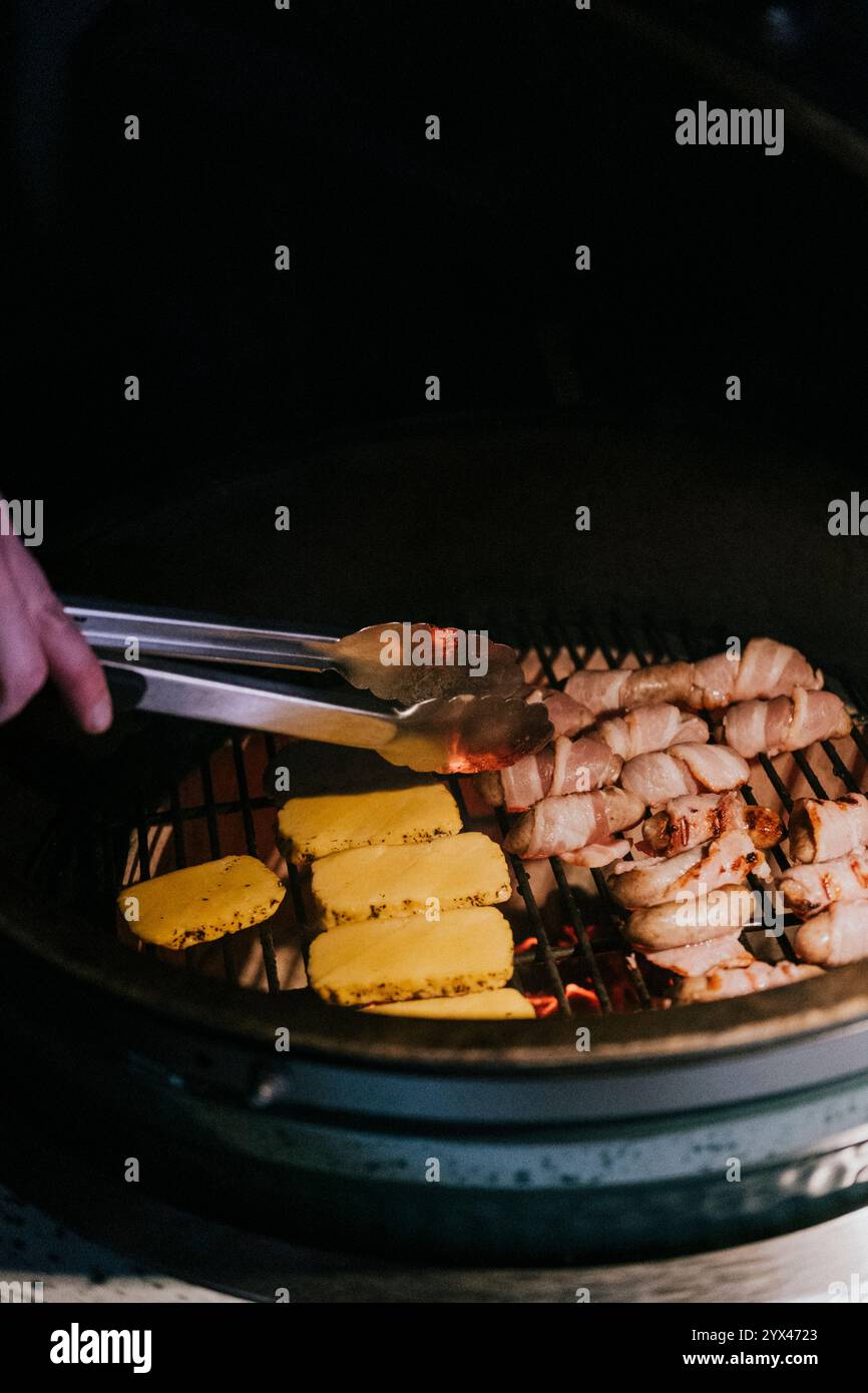 Eine Person kocht Essen auf einem Grill, einschließlich Huhn und Maisbrot. Die Person benutzt eine Zange, um das Essen umzudrehen Stockfoto