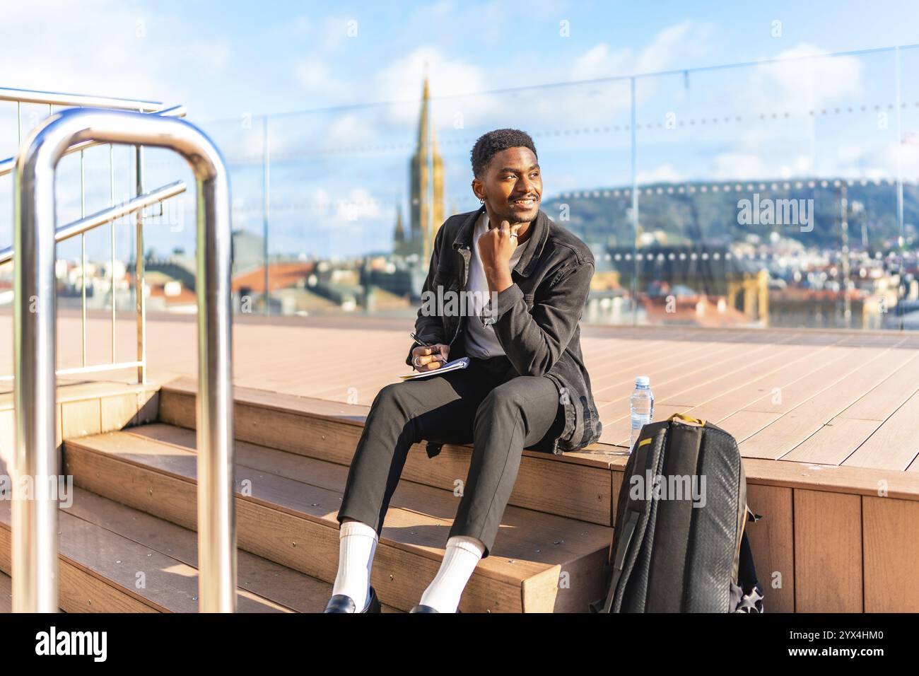 Glücklicher afrikanischer Mann, der von Hand in einem Notizbuch auf einem Dach mit Blick auf die Stadt skizziert Stockfoto