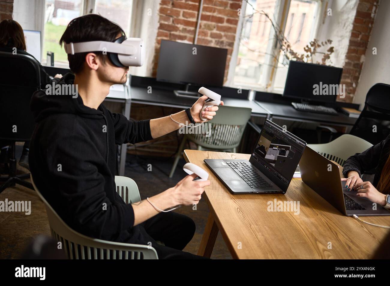In einem modernen Büro verwendet ein Mann ein Virtual-Reality-Headset mit Controllern, um Technologie und Innovation im Arbeitsumfeld zu präsentieren Stockfoto