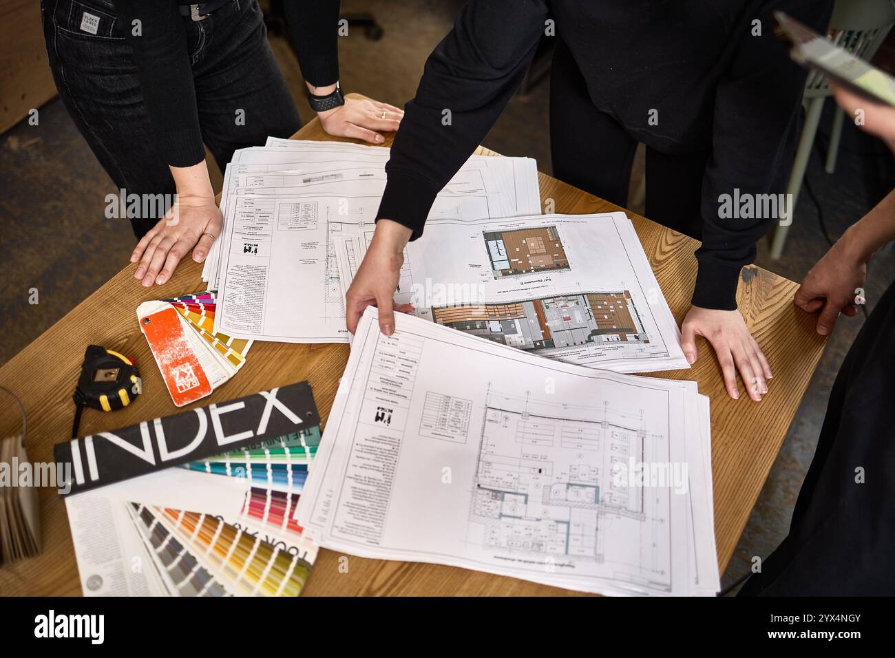 Team von Architekten, die Baupläne prüfen und Projektdetails an einem Schreibtisch besprechen, wobei die Zusammenarbeit beim Architekturkonzept betont wird Stockfoto