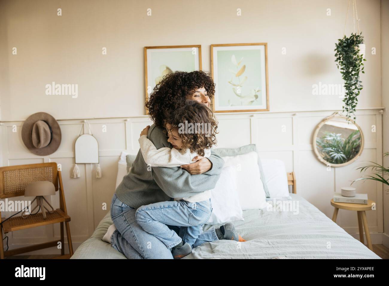 Eine warme und herzliche Szene, in der eine Mutter ihr Kind liebevoll umarmt, spielt in einem hellen Schlafzimmer und zeigt ein Gefühl von Liebe, Komfort und familiärer Bindung Stockfoto