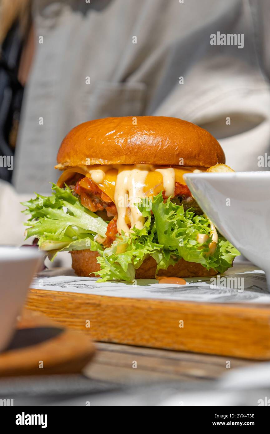 Saftiger Hamburger mit viel tropfender Sauce, Käse und Salat. Nicht gesund, aber sehr leckeres kalorienreiches Essen. Straßenmahlzeit, kein inszenierter Fotomburger Stockfoto