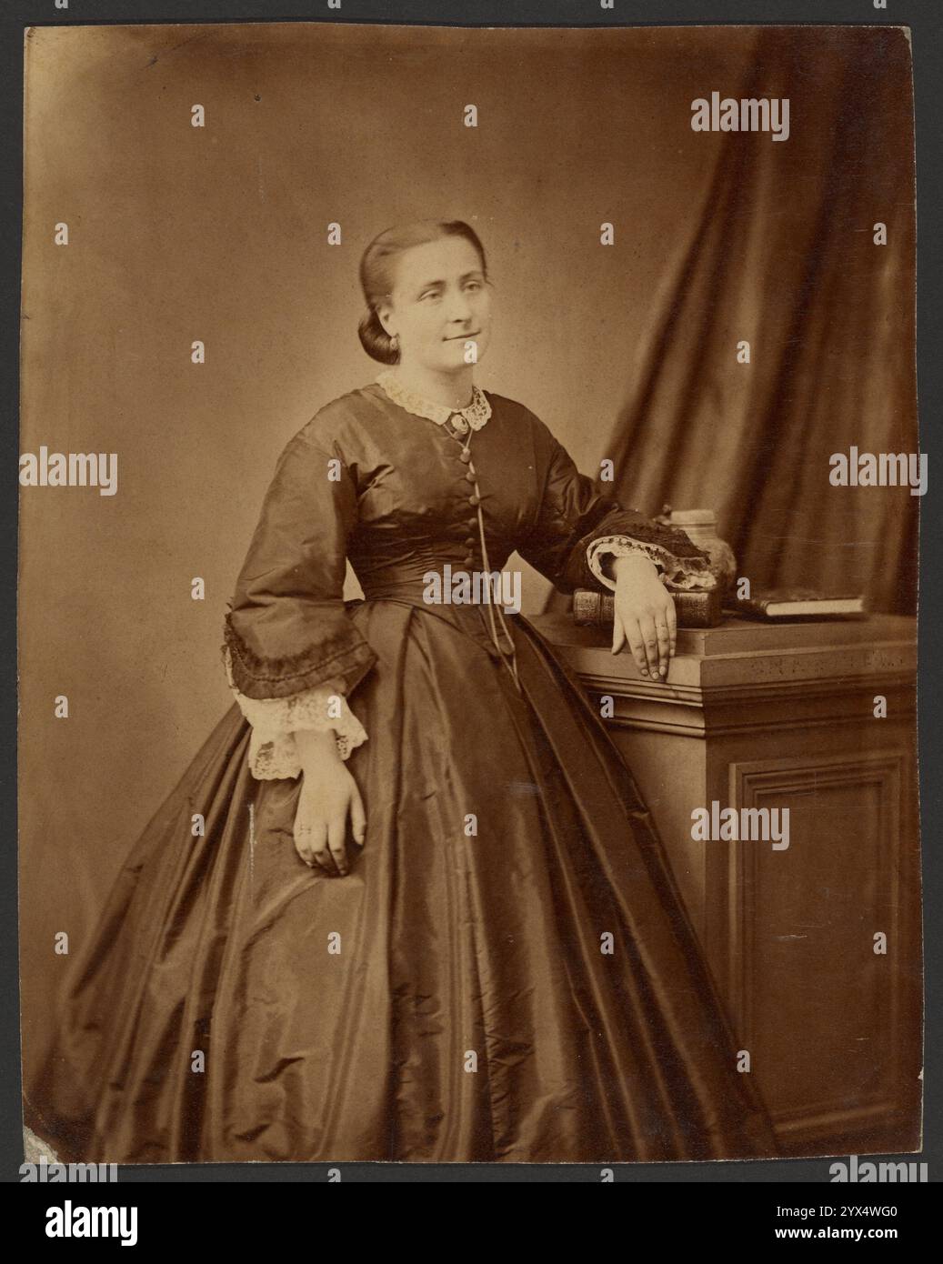 Porträt einer Frau, um 1860-1869. Zusätzliche Info: Porträt einer Frau in voller Länge, die mit einem Arm auf einem kurzen Stapel Bücher steht. Die Frau trägt ein einfarbiges Kleid mit durchgehendem Rock und breiten Ärmeln. Sie trägt Spitzenunterärmel und trägt eine lange Kette. Stockfoto