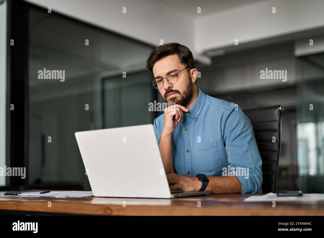 Junger beruflicher, beschäftigter Geschäftsmann, der auf Computer bei der Arbeit denkt. Stockfoto