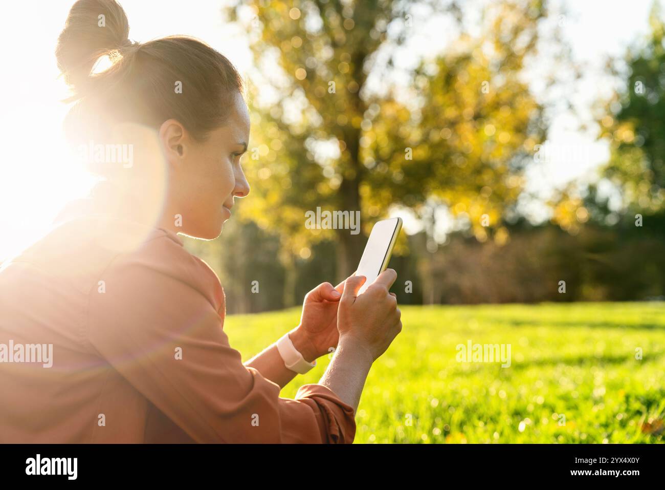 Stadtfrau, die auf dem Smartphone SMS sendet, während sie sich auf dem Rasen im Stadtpark entspannt. Stockfoto