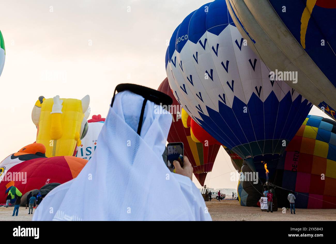 Doha, Katar. Dezember 2024. Die Menschen machen Fotos von Heißluftballons, die bei Sonnenaufgang während des Qatar Balloon Festival 2024 in Doha, Katar, am 13. Dezember 2024 abheben. Die 5. Auflage des Qatar Balloon Festivals findet vom 12. Bis 22. Dezember statt, an dem mehr als 50 Teilnehmer teilnehmen. (Foto: Noushad Thekkayil/NurPhoto) Credit: NurPhoto SRL/Alamy Live News Stockfoto