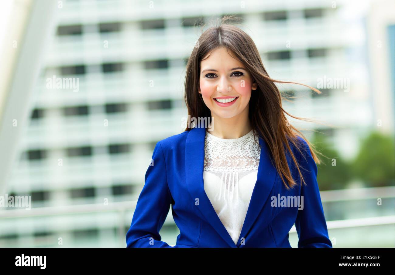 Die junge Geschäftsfrau in einem blauen Blazer lächelt in einem modernen Stadtumfeld selbstbewusst und zeigt ein professionelles und erfolgreiches Image Stockfoto