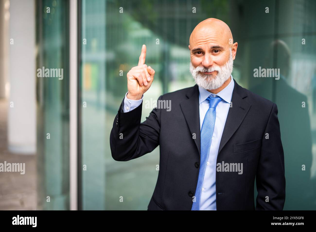 Ein leitender Geschäftsmann in einem scharfen Anzug lächelt und hebt selbstbewusst seinen Zeigefinger, was eine neue Idee in einem modernen Bürogebäude signalisiert Stockfoto
