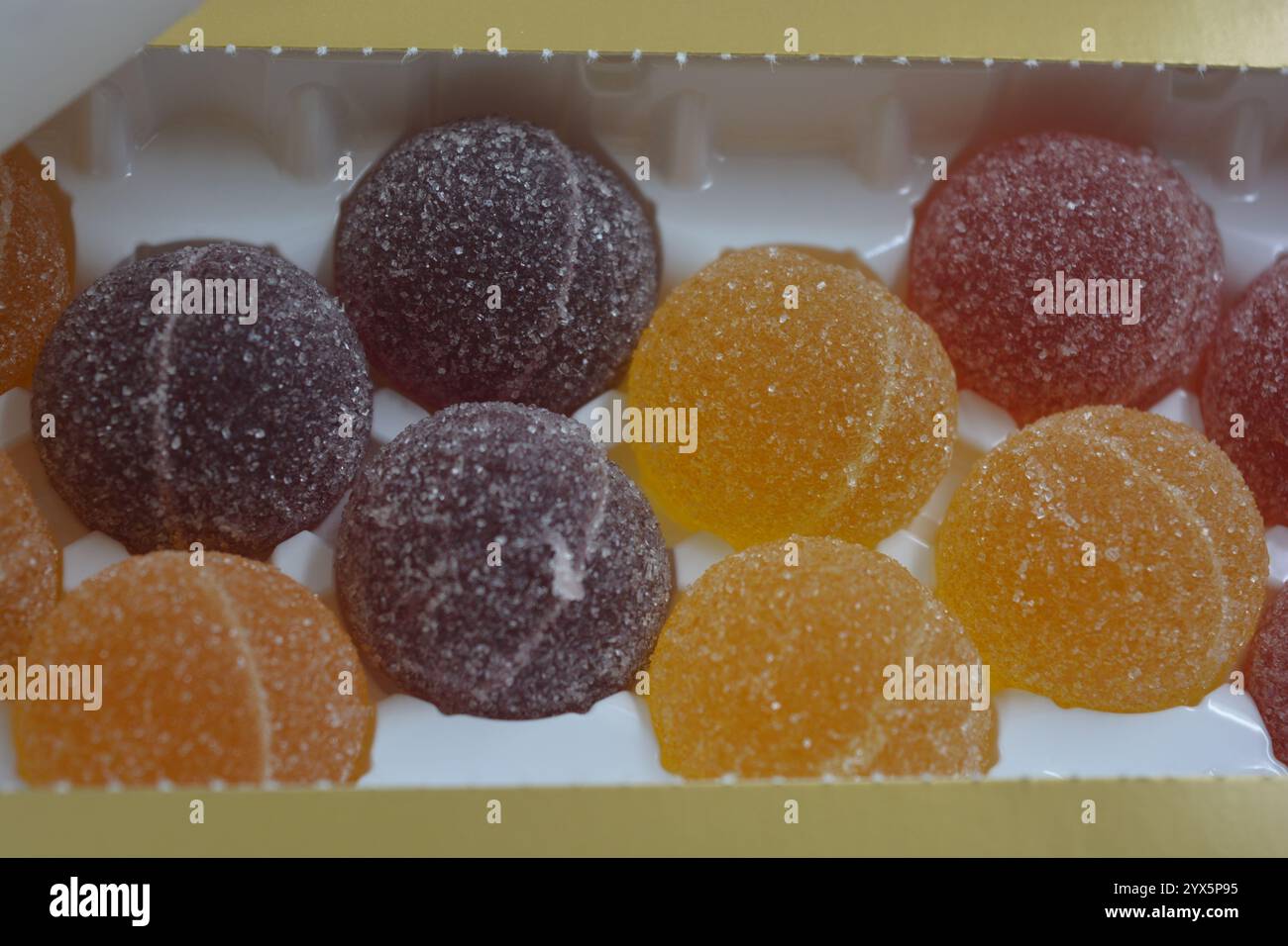 Originale finnische Gelee-Bonbons in Form von runden Kugeln, die mit weißem Zucker bedeckt sind. Gelbe, orange, kirschrote, gummiartige Bonbons sind in weißer Verpackung. Stockfoto