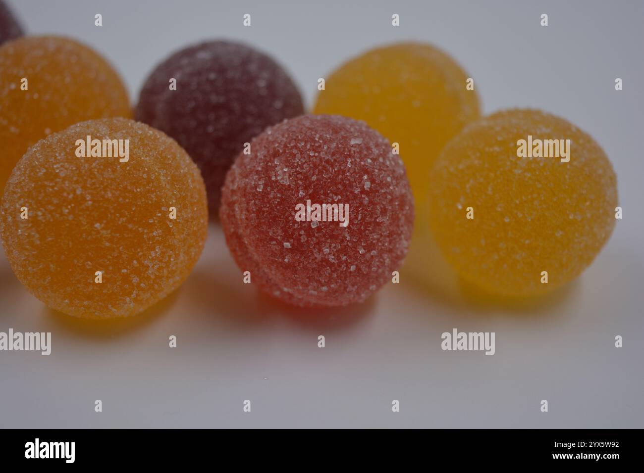 Originale finnische Gelee-Bonbons in Form von runden Kugeln, die mit weißem Zucker bedeckt sind. Gelbe, orange, kirschrote, gummirote Bonbons sind auf einem weißen Plastik. Stockfoto