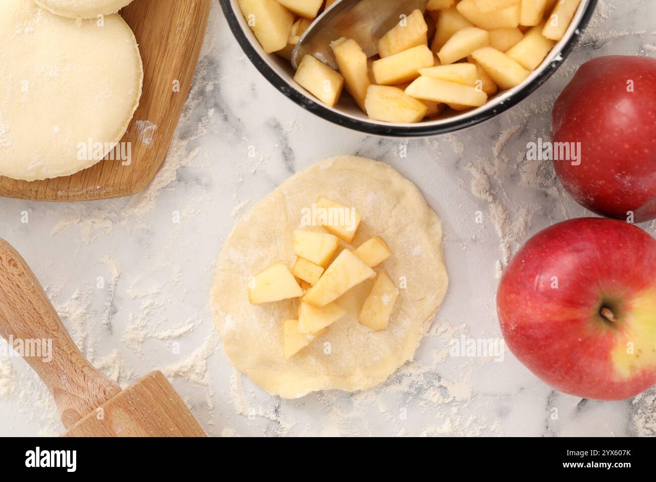 Pirozhki (gefüllte Teigtaschen). Teigstücke mit Äpfeln auf weißem Marmortisch, flach gelegt Stockfoto Pirozhki (gefüllte Teigtaschen). Teigstücke mit Äpfeln auf weißem Marmortisch, flach gelegt Stockfoto
