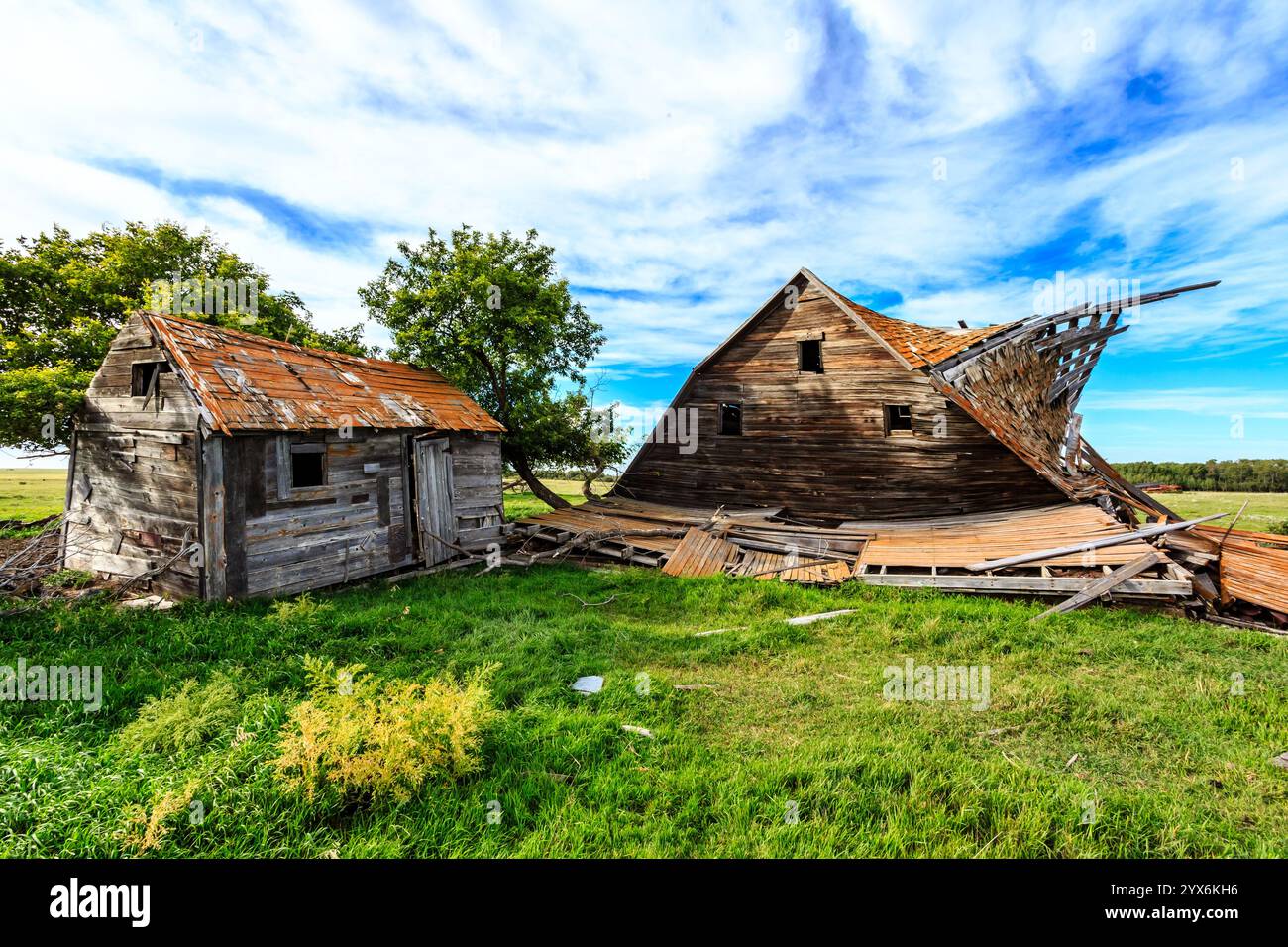 Ein baufälliges altes Haus liegt auf einem grasbewachsenen Feld. Das Haus ist in einem Zustand der Verwerfung, ein großer Teil des Daches fehlt. Das Konzept des Verlassens Stockfoto