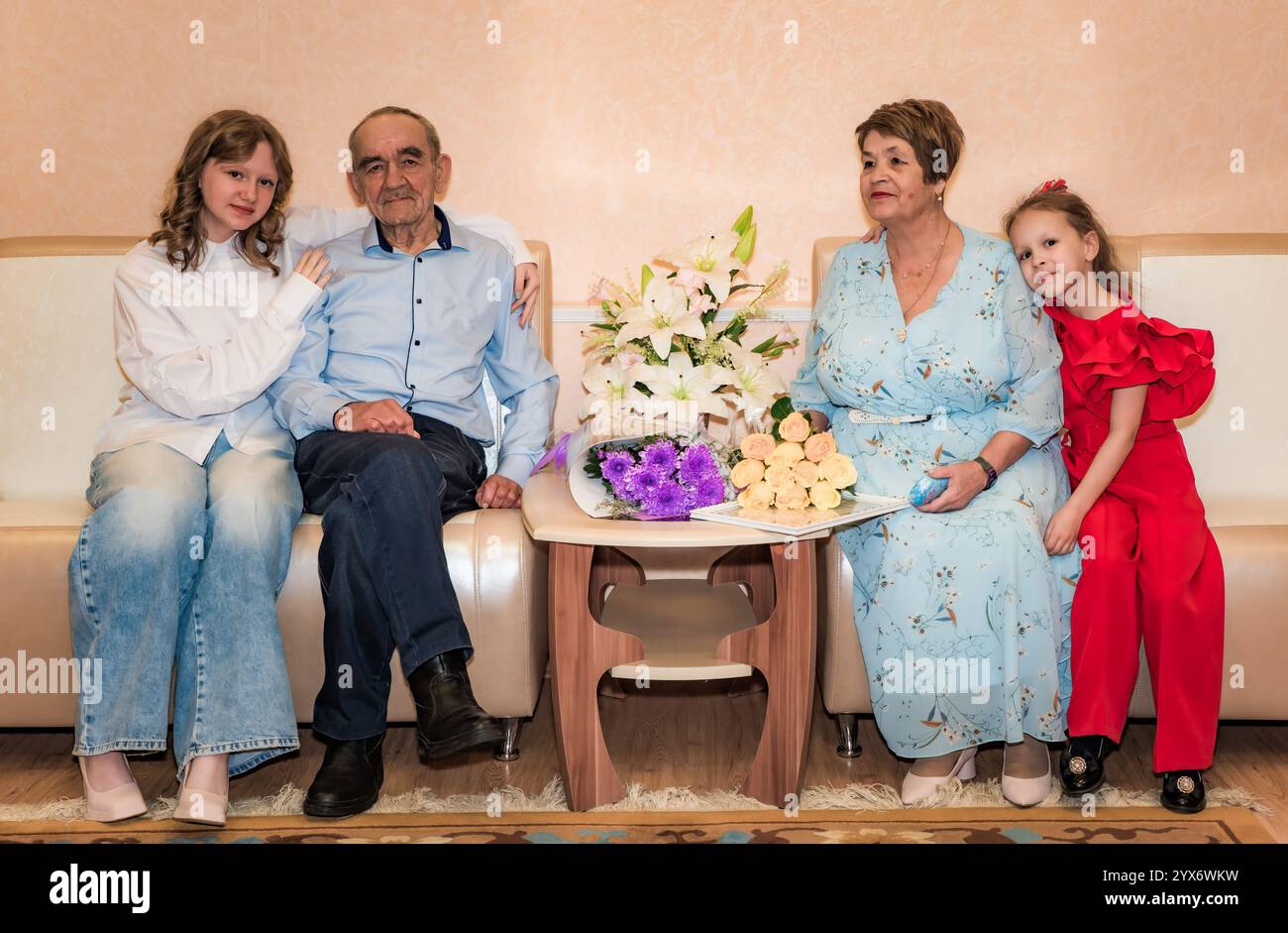 Zwei Enkelinnen sitzen mit ihren russischen Großeltern und feiern ihren 50. Goldenen Hochzeitstag. Die Familie sitzt auf einem Sofa, umgeben Stockfoto