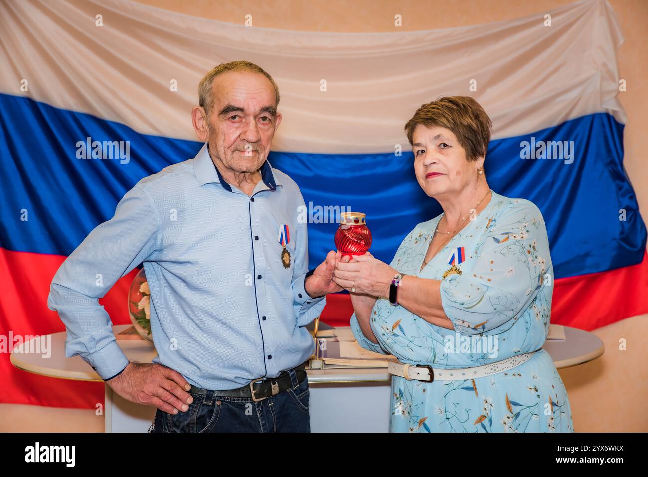 Älteres russisches Ehepaar feiert ihren goldenen Hochzeitstag in einem Standesamt, steht vor russischer Flagge und hält ein Orthodo Stockfoto