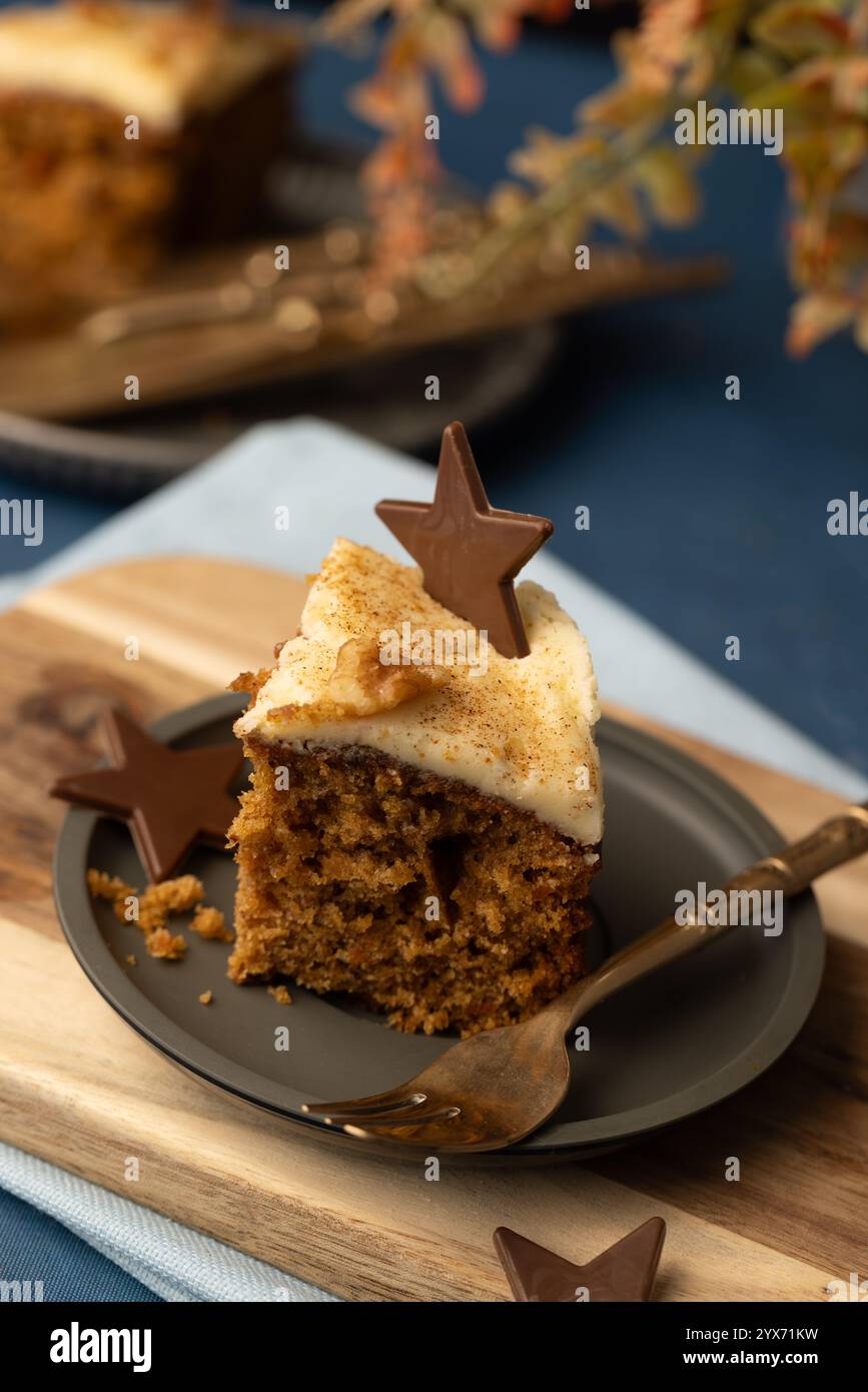 Ein Stück Karottenkuchen mit cremigem Zuckerguss und sternförmigem Schokoladendeckel, serviert auf einem kleinen Teller mit Gabel, der Hintergrund ist mittelblau Stockfoto