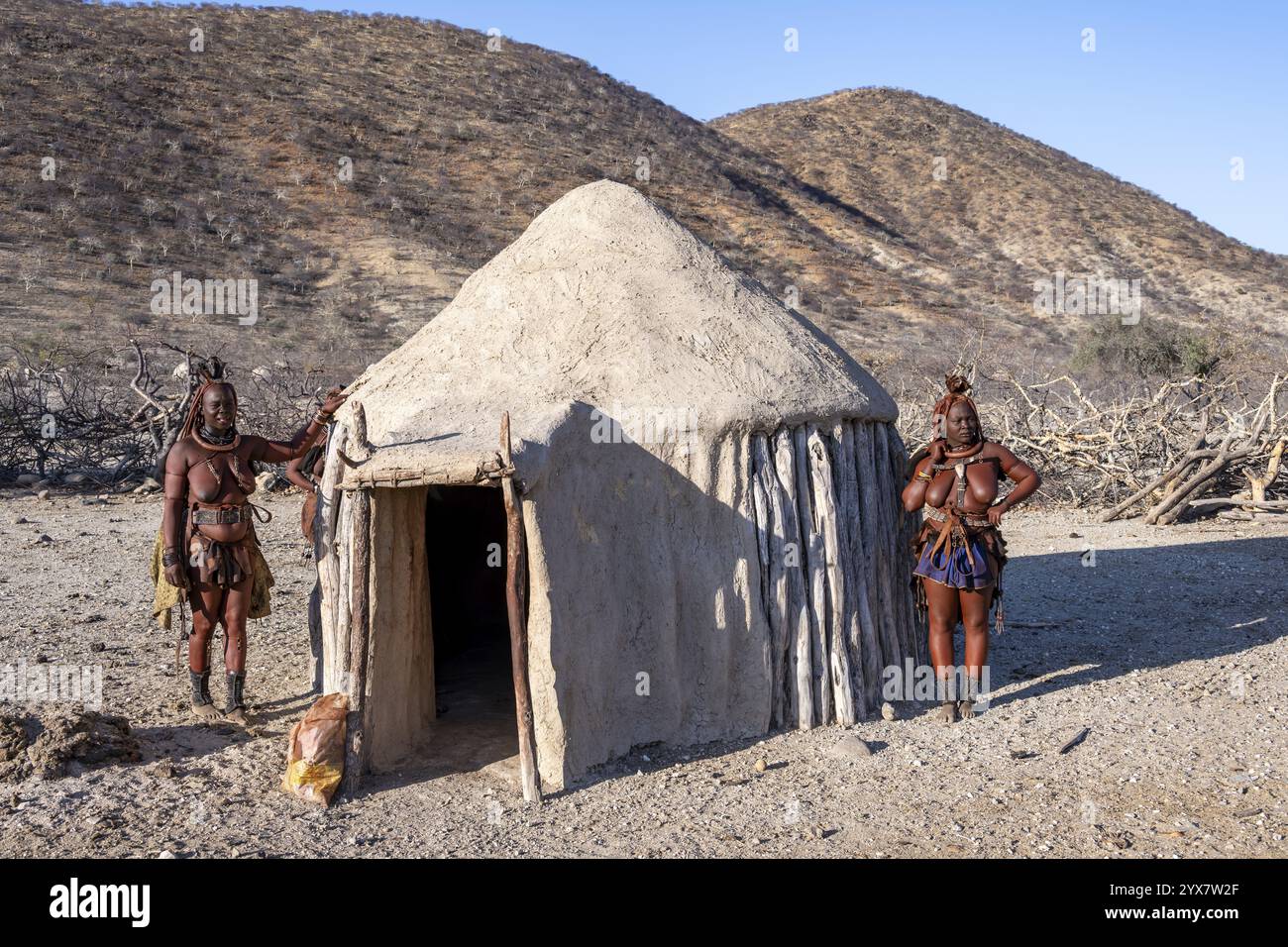 Die verheiratete Himba-Frau lehnt sich an ein traditionelles Lehmhaus, traditionelles Himba-Dorf, Kaokoveld, Kunene, Namibia, Afrika Stockfoto