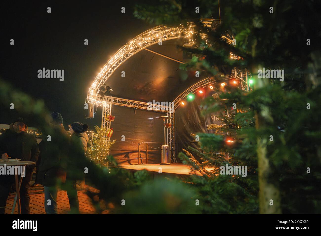 Nachtaufnahme einer beleuchteten Weihnachtsbühne mit Menschen, umgeben von festlichen Tannen, Weihnachtsmarkt, Nagold, Schwarzwald, Deutschland, Europa Stockfoto