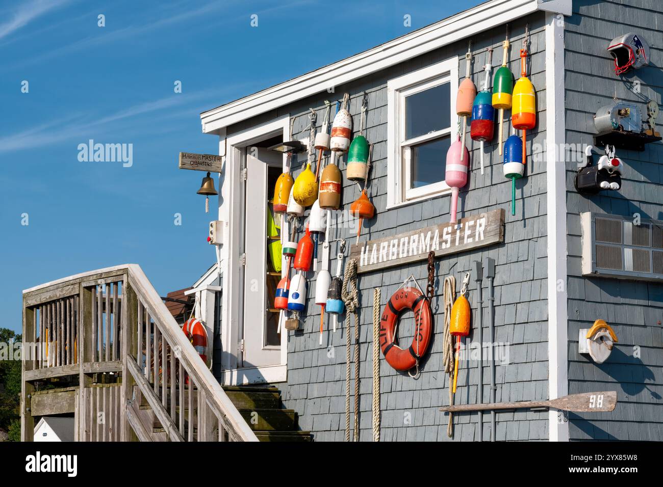 Farbenfrohe Bojen und ein Rettungsschirm schmücken das Äußere eines Hafenmeisters und bilden einen Kontrast zu seinem blauen Abstellgleis. Eine Holztreppe führt hinauf Stockfoto