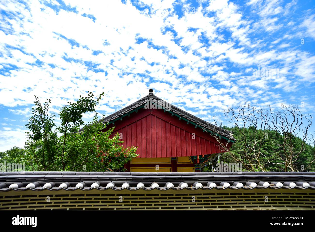 Ein rotes Gebäude mit rotem Dach. Das Dach ist mit Fliesen bedeckt. Das Gebäude ist von Bäumen umgeben Stockfoto