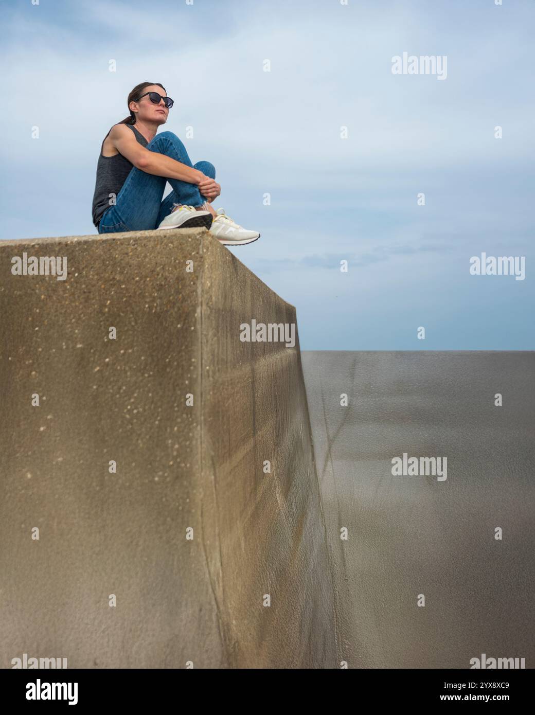 Frau, die draußen auf einer Betonmauer sitzt Stockfoto