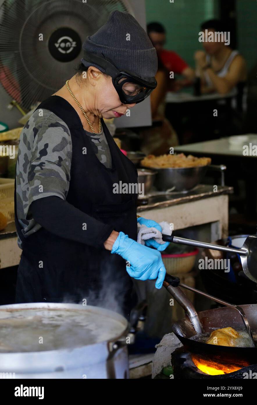 Bangkok, Thailand - 20. April 2023: Der mit einem Michelin-Stern ausgezeichnete Küchenchef Jay Fai, trägt ihre Schutzbrille und bereitet ihr klassisches Krabbenomelett vor. Stockfoto