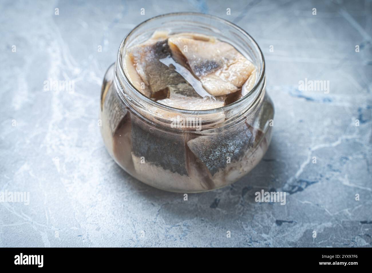 Marinierter Hering in einem Glasgefäß auf einem grauen Marmortisch. Hochwertige Fotos Stockfoto