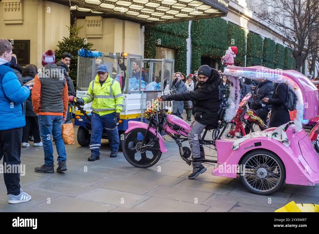 Fahrradpark mit Rikscha-Taxis auf dem Bürgersteig vor dem Kaufhaus Selfridges in einer belebten Oxford-Straße, die vor Weihnachten auf Kunden wartet. London, Großbritannien. Stockfoto
