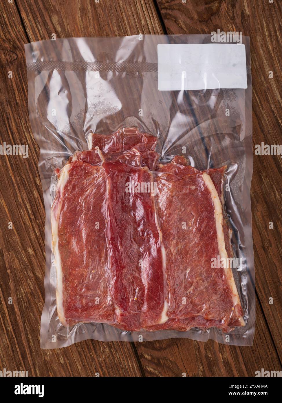 Schweinefleischchips in transparenter Vakuumverpackung auf Holztisch, Draufsicht Stockfoto