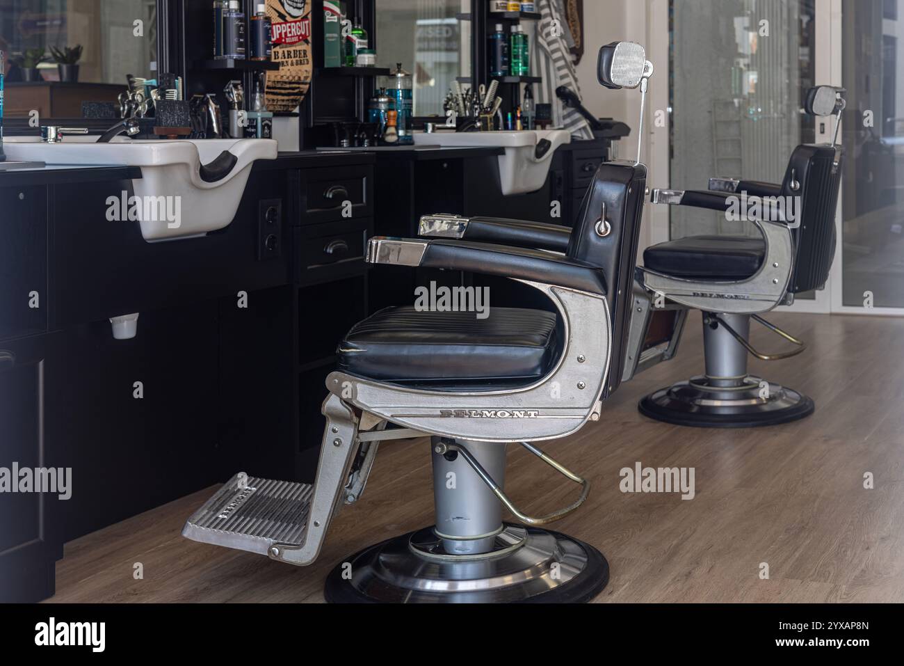 Zwei Belmont Friseurstühle an eleganten schwarzen Arbeitsplätzen mit eingebauten Waschbecken und Pflegeutensilien in einem stilvollen und professionellen Friseurladen. Stockfoto