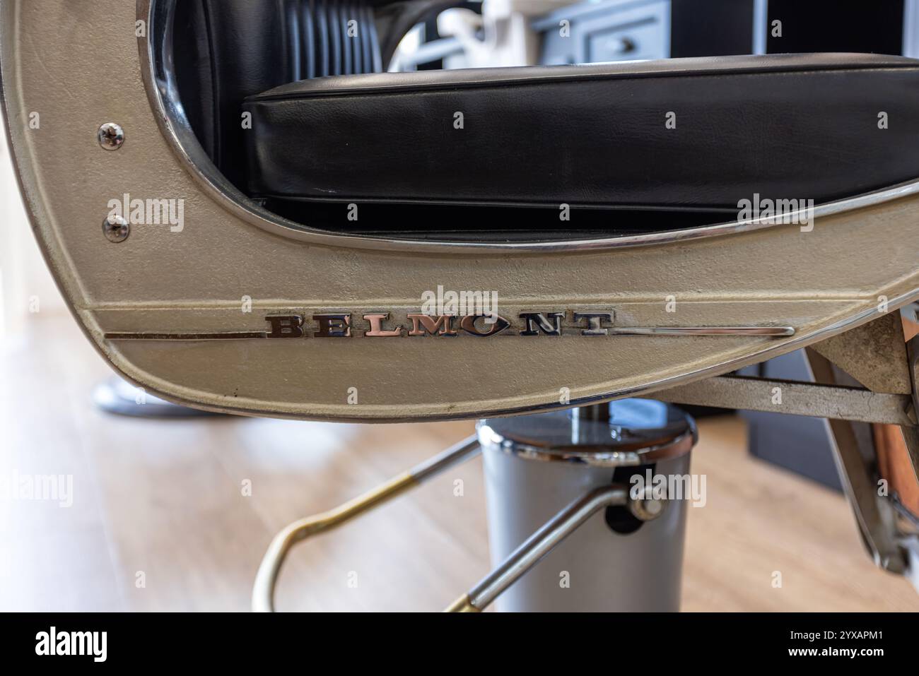 Detaillierter Blick auf den metallischen Rahmen eines Barbierstuhls von Belmont, mit Handwerkskunst, schwarzem Ledersitz und Retro-Design in einem modernen Friseurladen. Stockfoto