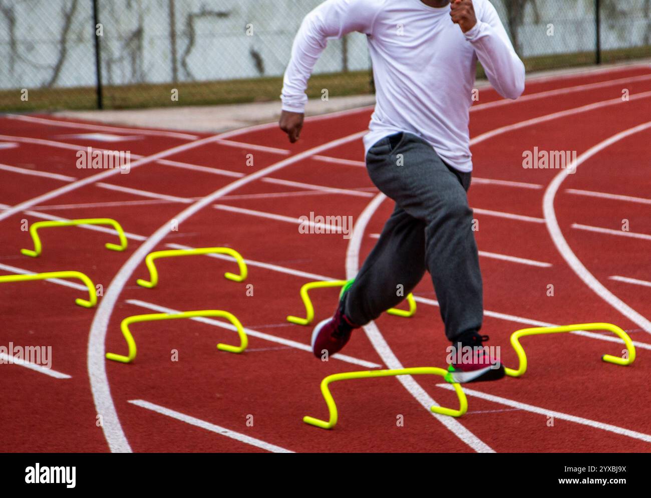 Der Athlet trainiert intensiv auf einer roten Strecke und überwindet Hürden während Agilitätsübungen, um die Leistung zu verbessern. Stockfoto