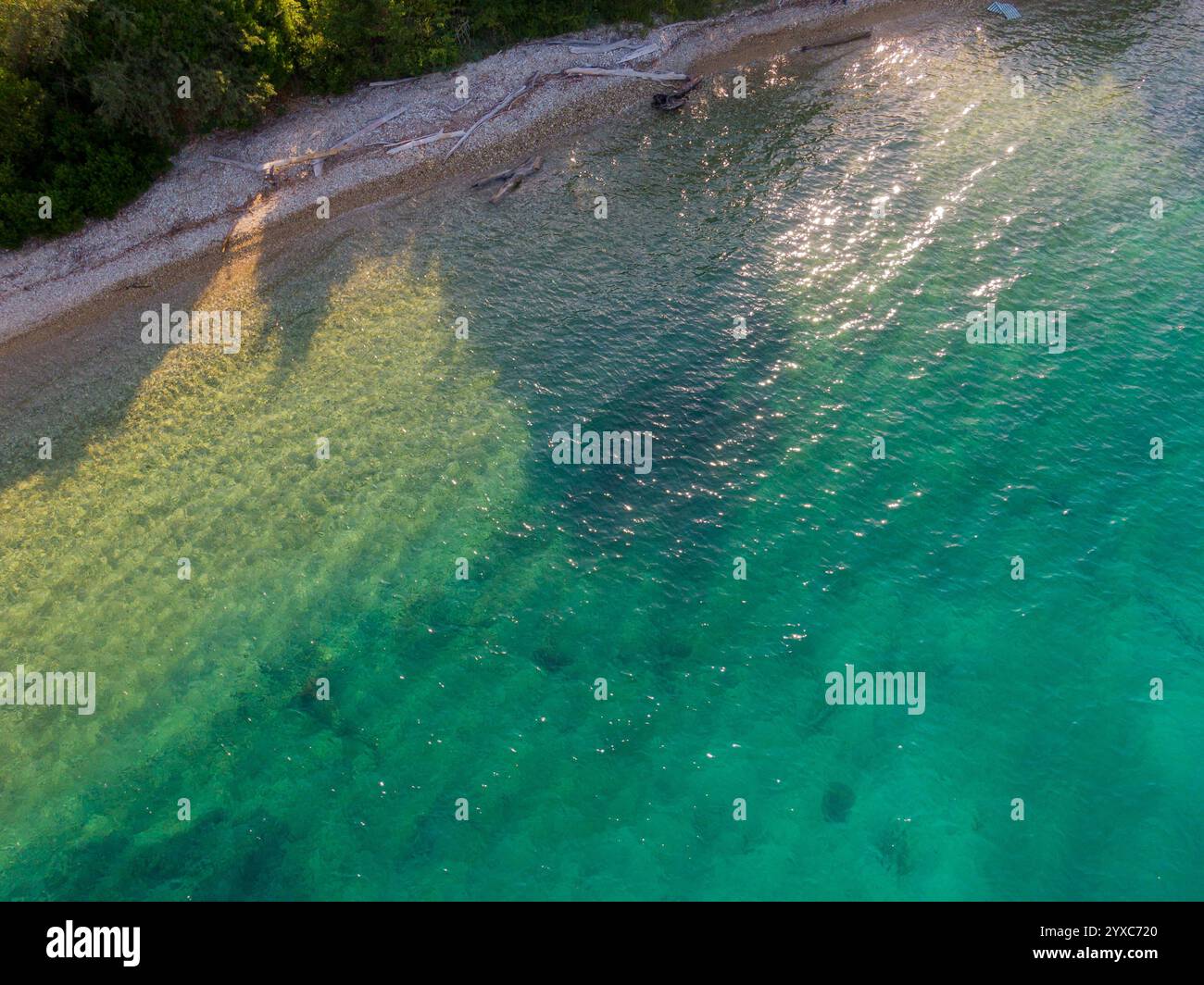 Bei dieser Aussicht aus der Vogelperspektive trifft das ruhige türkisfarbene Wasser auf ein Kieselstrand. Stockfoto