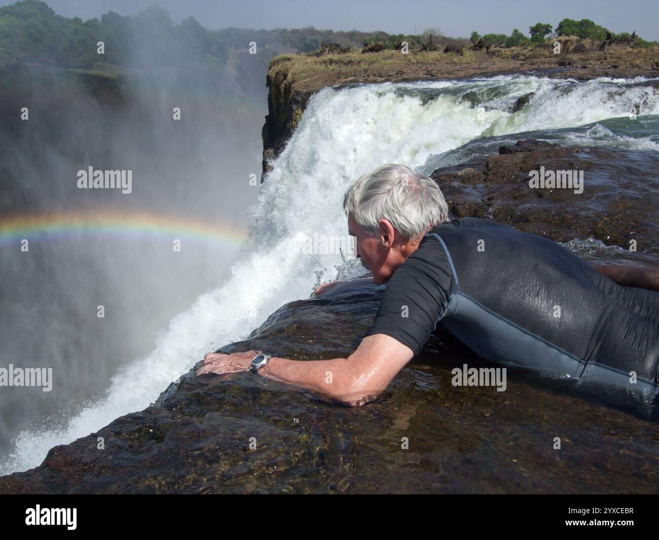 Senior Mann liegt im Wasser und blickt über den Rand der Victoria Falls bei Devil's Pool, Livingstone Island, Sambezi River, Sambia, Afrika Stockfoto