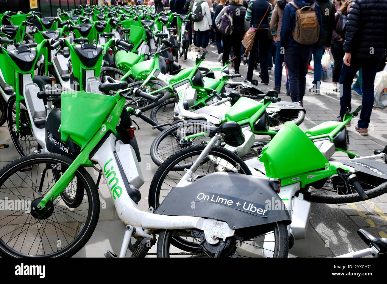 Fußgänger, die einen Haufen Lime-Elektrofahrräder vermeiden, die auf dem Bürgersteig am Eingang zur Craven Street on Strand in Central London umfallen. Stockfoto