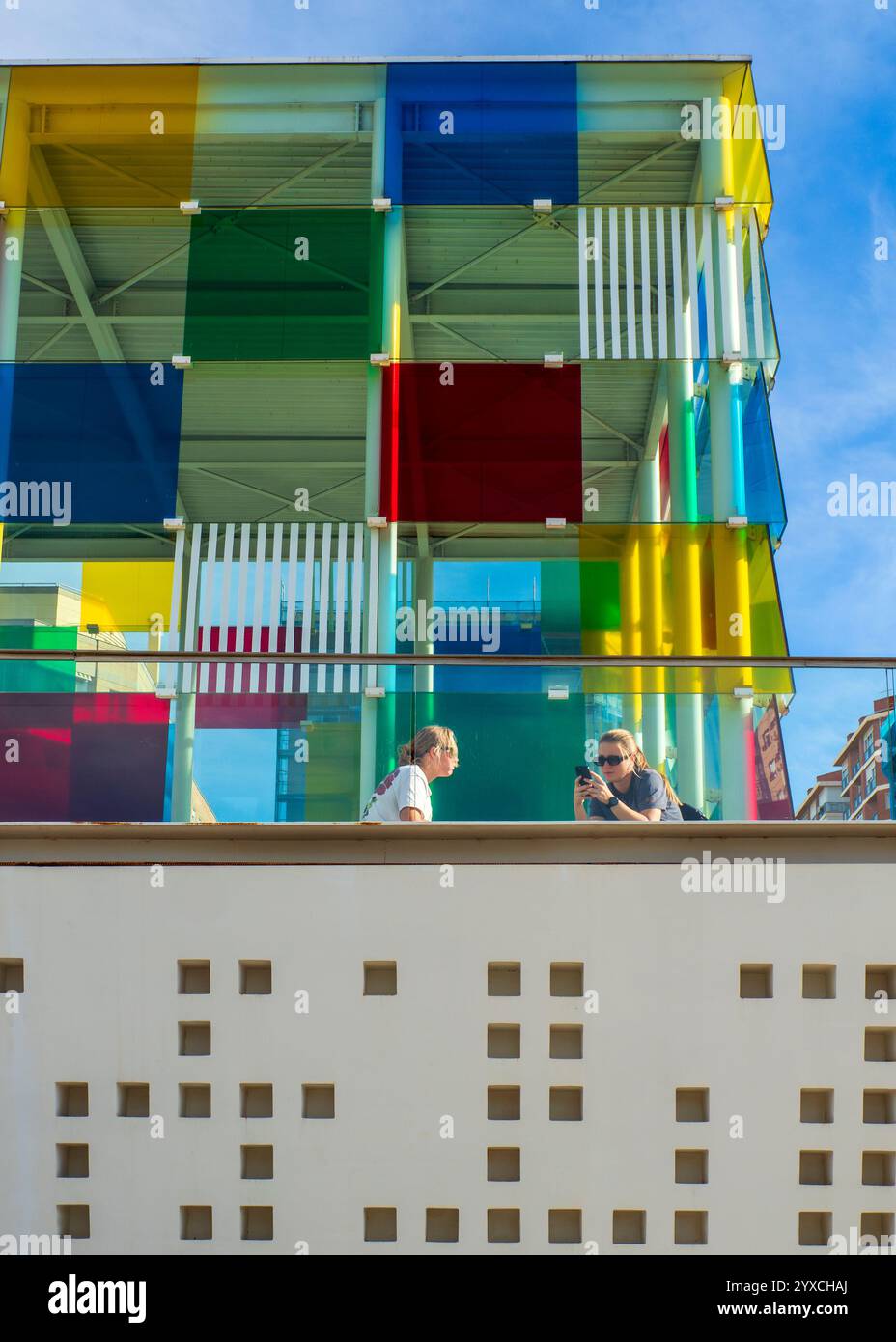 12/07/2024. Malaga, Spanien. Zwei junge Mädchen sitzen neben der Fassade des Pompidou Museums in Malaga. Stockfoto