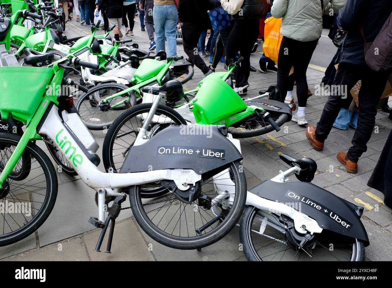 Fußgänger, die einen Haufen Lime-Elektrofahrräder vermeiden, die auf dem Bürgersteig am Eingang zur Craven Street on Strand in Central London umfallen. Stockfoto