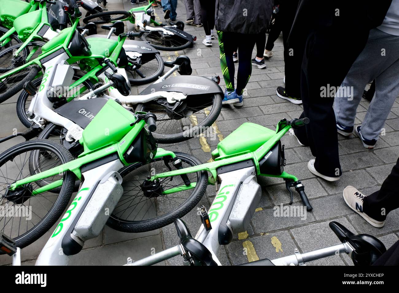 Fußgänger, die einen Haufen Lime-Elektrofahrräder vermeiden, die auf dem Bürgersteig am Eingang zur Craven Street on Strand in Central London umfallen. Stockfoto