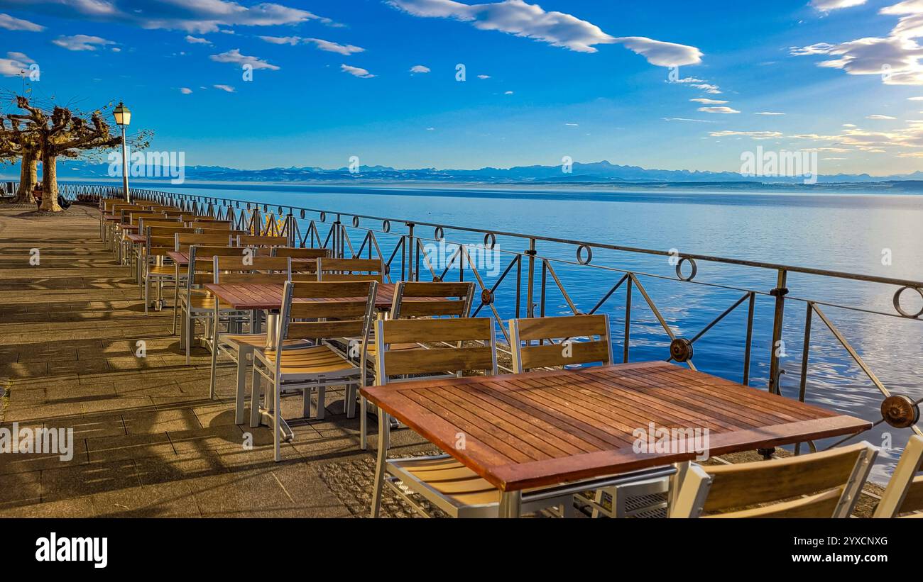 Promenade in Meersburg mit spannendem Blick auf den Bodensee, die Schweiz und die Alpen an einem sonnigen Wintertag. Leere Tische auf dem Stuhl am Ufer von Stockfoto
