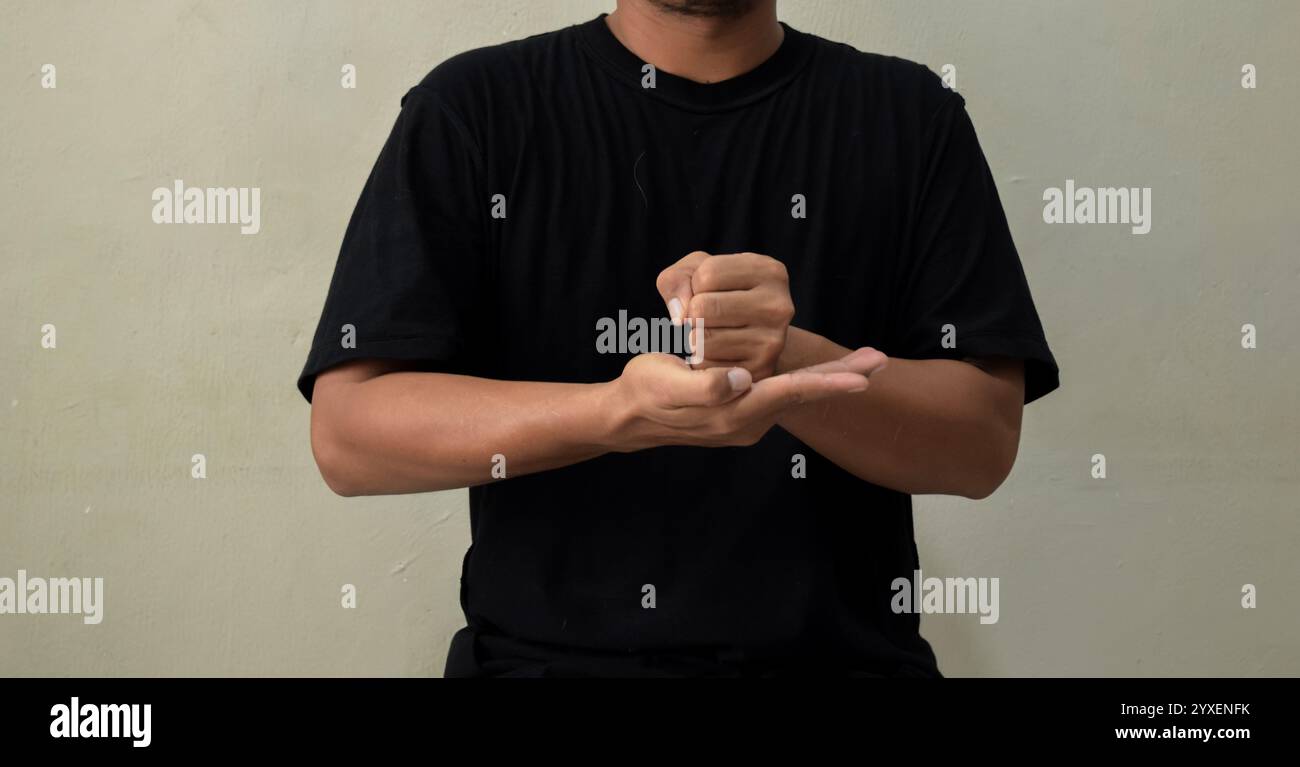 Junger Mann, der das Wort KREUZIGT in Gebärdensprache auf grauem Hintergrund zeigt Stockfoto