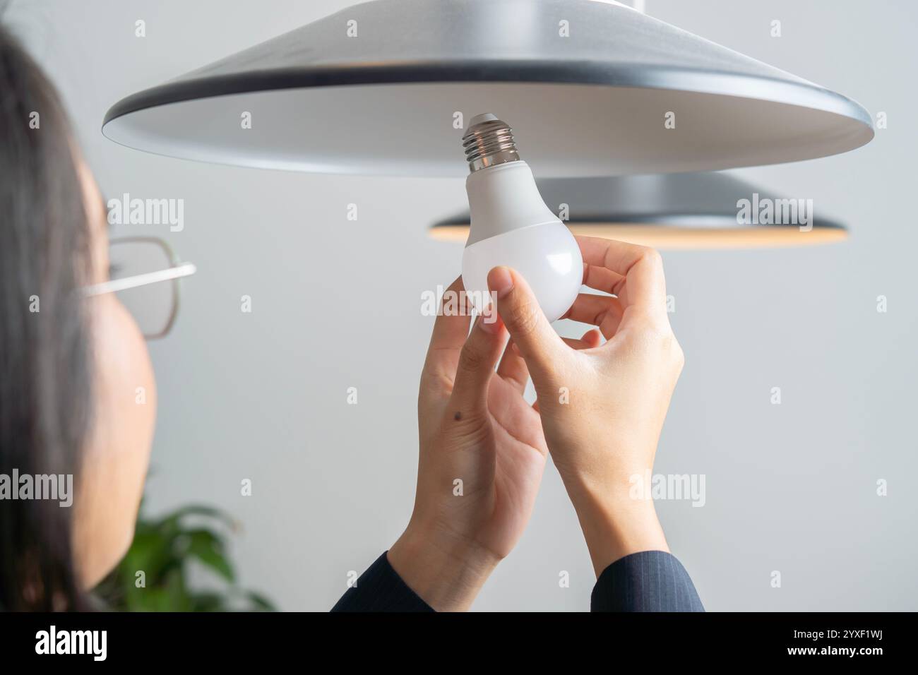 Rückansicht einer asiatischen Frau, die zu Hause eine kaputte Glühbirne in LED umwandelt. Selektiver Fokus auf die Hände. Stockfoto