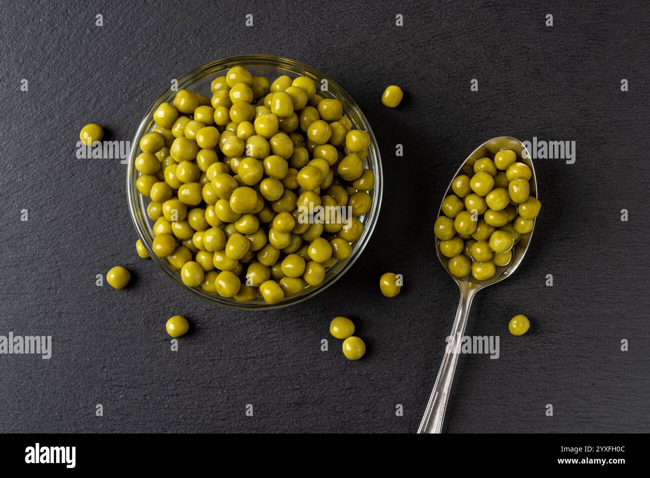 Schüssel mit grünen Erbsen aus der Dose auf schwarzem Hintergrund. Nass marinierte Süßerbsen in einer Glasschale und einem Metalllöffel. Das Konzept des pflanzlichen Proteins. Stockfoto