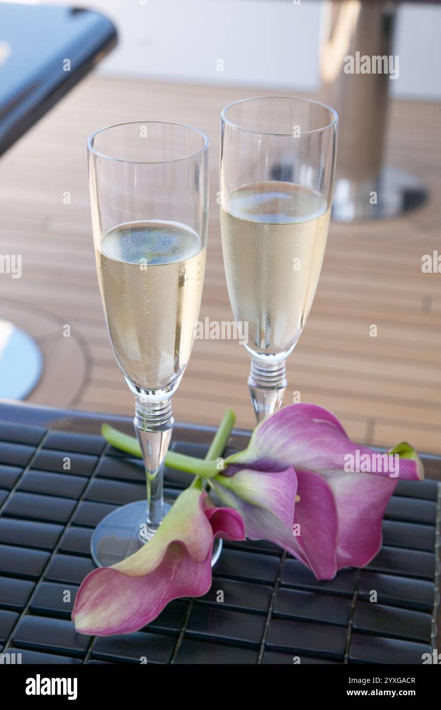 Schicke Gläser Champagner, begleitet von zarten lila Blumen auf einer stilvollen Oberfläche, die Romantik und Feier verkörpern. Stockfoto
