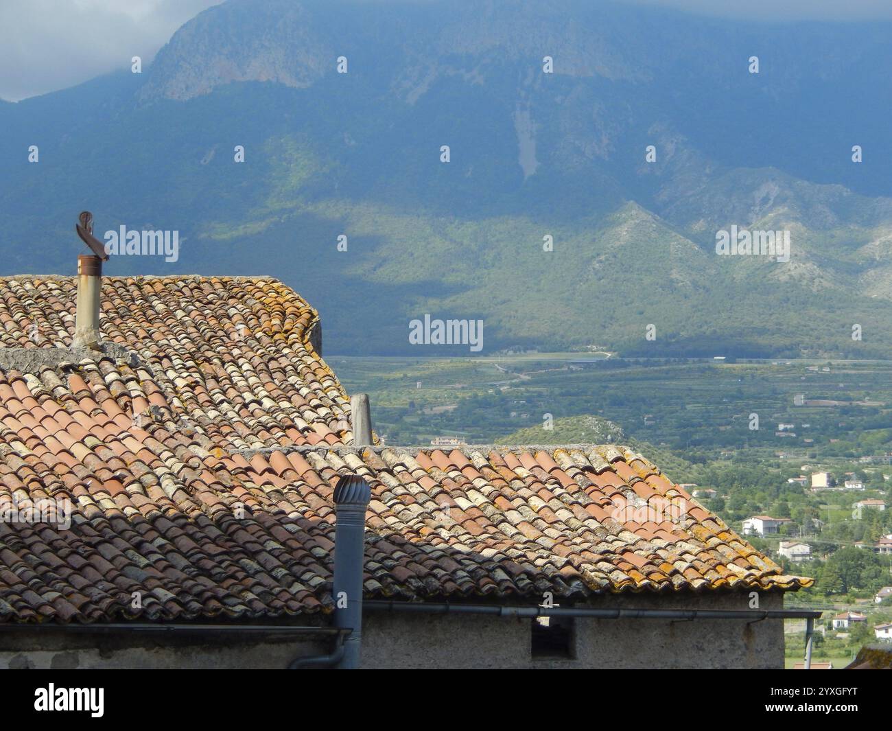 Verwitterte Terrakotta-Dachziegel decken ein Gebäude in ländlicher Umgebung mit einer majestätischen Bergkette im Hintergrund Stockfoto