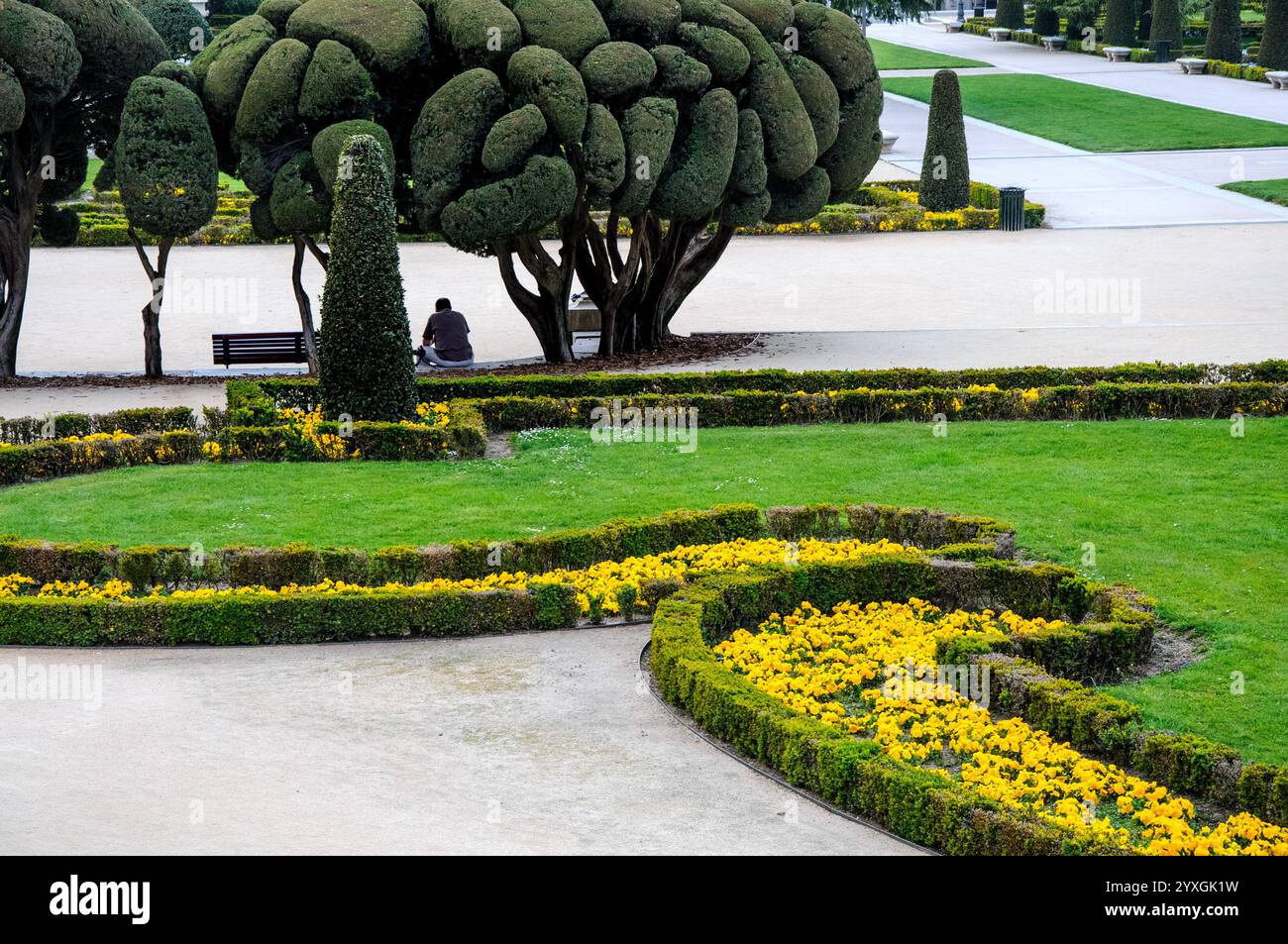 Madrid, Spanien. Parque del Buen Retiro/Retiro Park. Mann, der allein unter Bäumen sitzt, in den formellen Gärten Stockfoto
