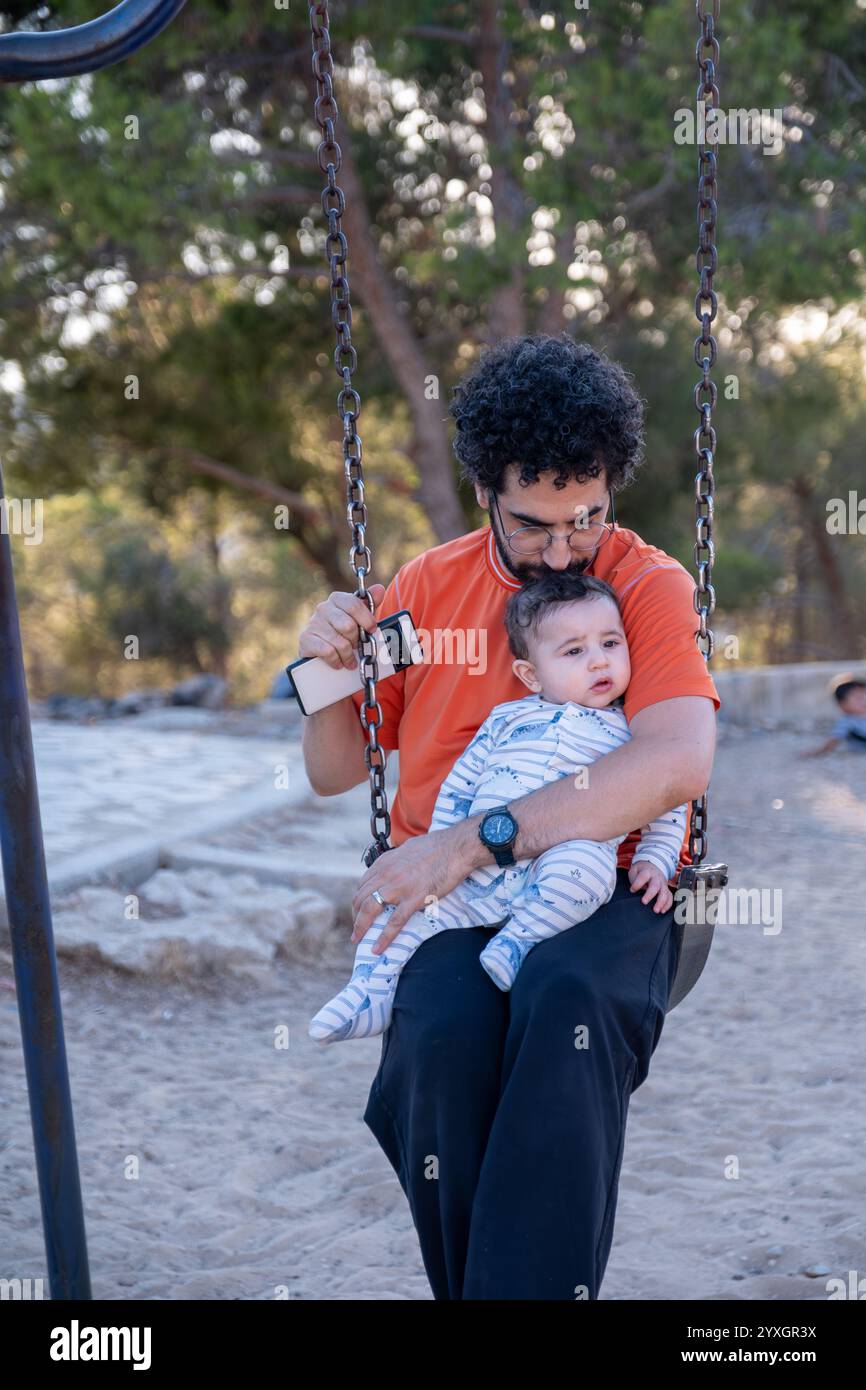 Ein ehrlicher Moment, der im Park festgehalten wird, während Vater und Kind eine friedliche Pause auf der Schaukel verbringen und die einfachen Freuden der Familie im Freien verkörpern. Stockfoto