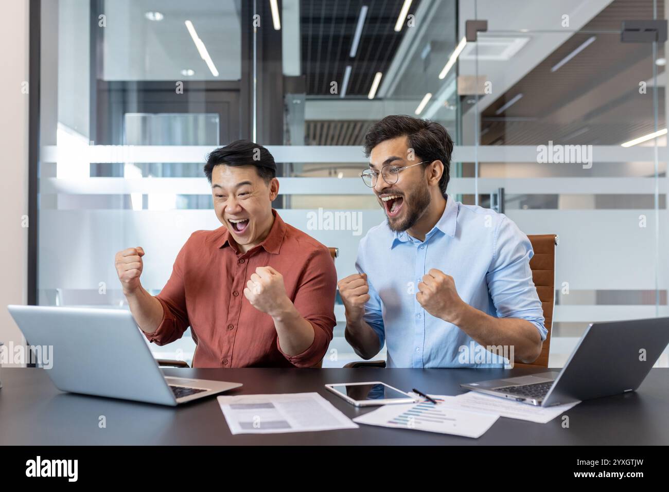 Zwei begeisterte Profis feiern einen Sieg während der Zusammenarbeit im Büro. Ihre Ausdrucksformen vermitteln Spannung und Teamarbeit, was sie zu einem dynamischen und belebenden Moment macht. Stockfoto