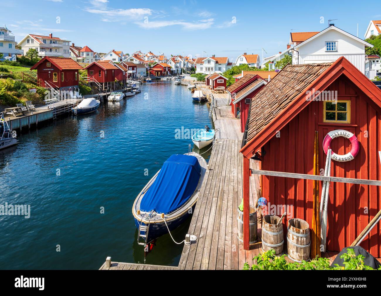 Blick auf das Dorf Grundsund in der Touristenprovinz Bohuslän, Schweden, mit weißen Häusern und roten Hütten auf beiden Seiten eines Kanals. Stockfoto