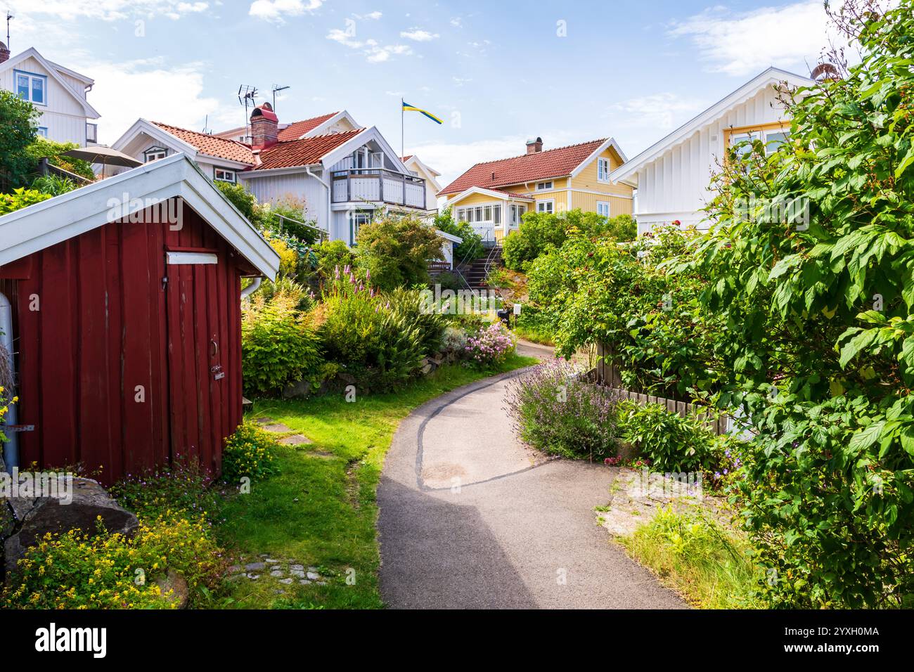Ein gepflasterter Weg schlängelt sich zwischen den Gärten der Holzhäuser des Dorfes Grundsund, typisch für die Touristenprovinz Bohuslän. Stockfoto