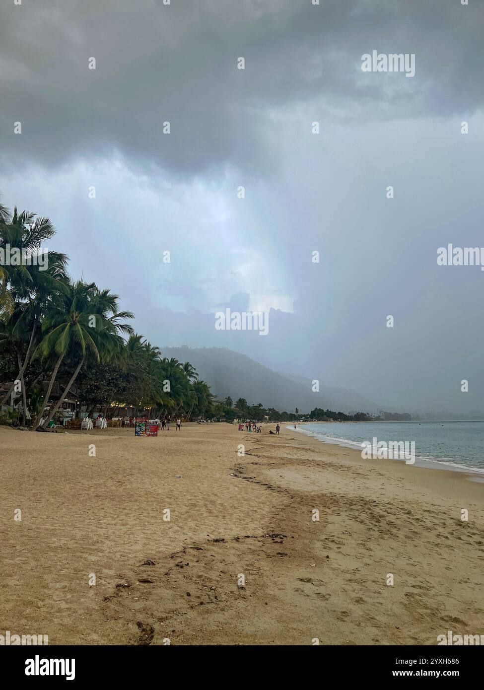 Starke Regenwolken nähern sich Lamai Beach mit nebeliger Bergkulisse, Palmen am Sandstrand und Strandbesucher entlang der Küste Stockfoto